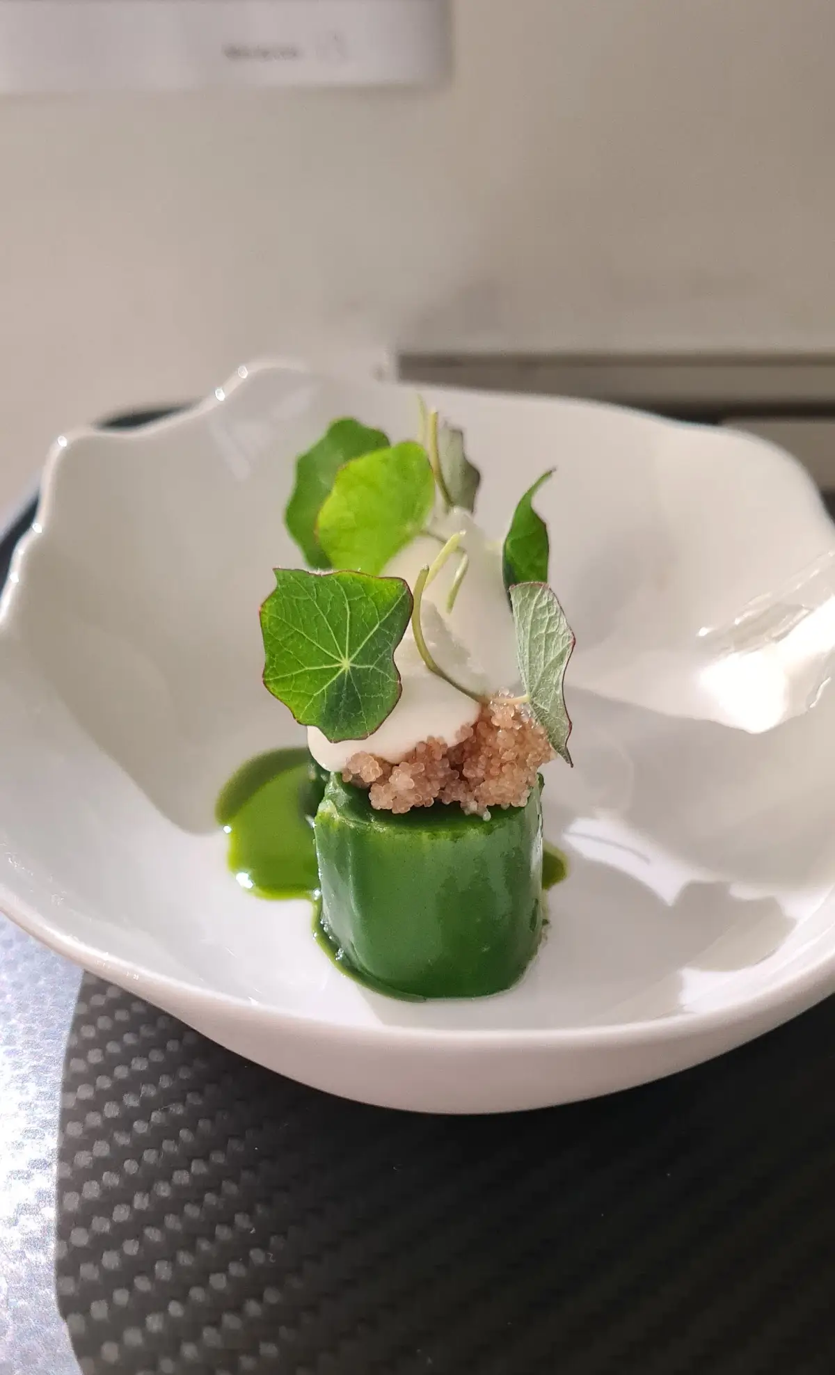 A gourmet dish at Restaurant Frederic Simonin, featuring a green vegetable roll topped with cream and microgreens.