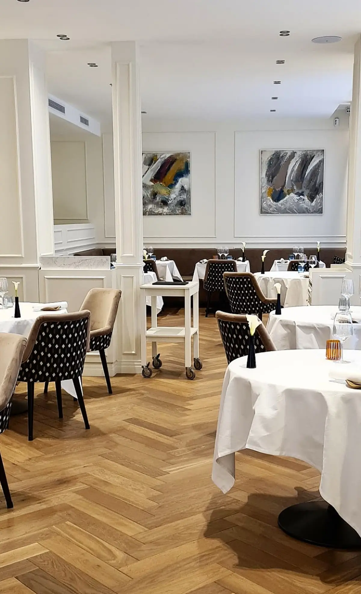 The elegant interior of Restaurant Frederic Simonin, an affordable Michelin star restaurant in Paris, featuring white tablecloths, patterned chairs, and modern art on the walls.