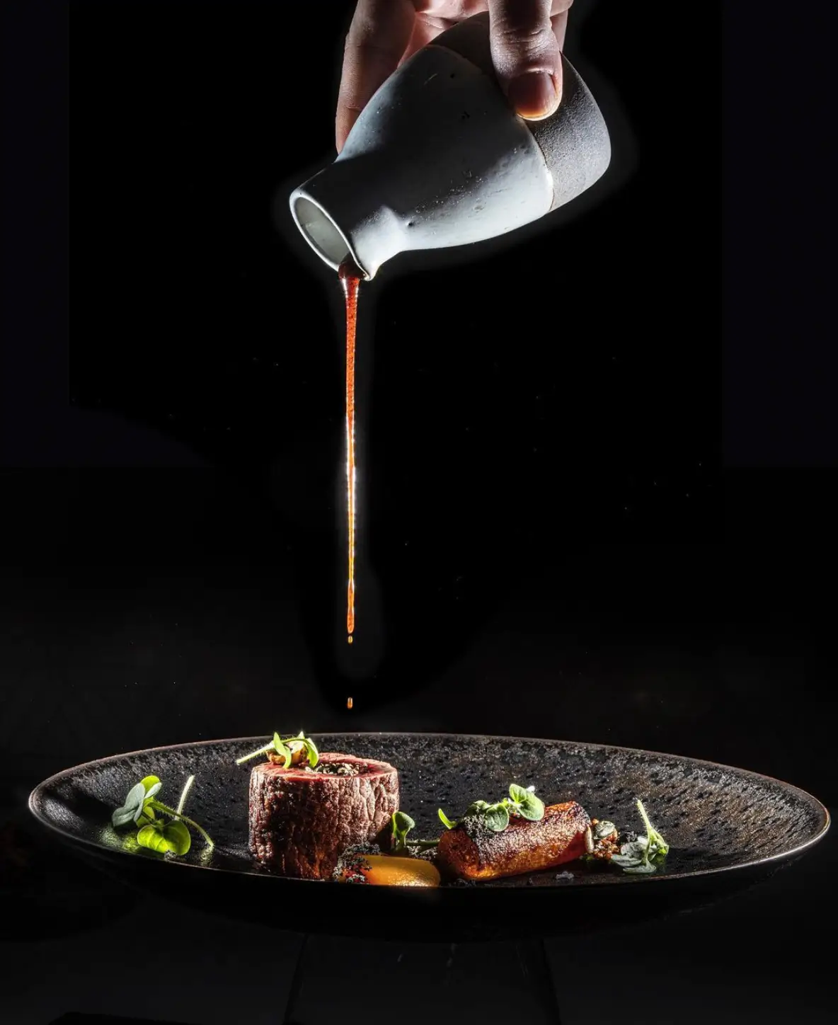 A hand pouring sauce over a gourmet dish at Restaurant H, highlighting fine dining at an affordable Michelin star restaurant in Paris