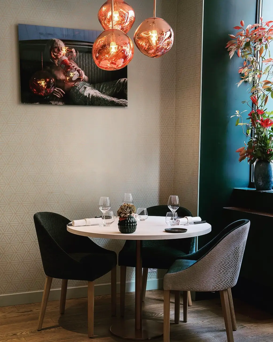 A cozy booth at Tomy & Co restaurant in Paris, an affordable Michelin star restaurant, with a round table set for dining, featuring a vibrant painting and lush green plant.