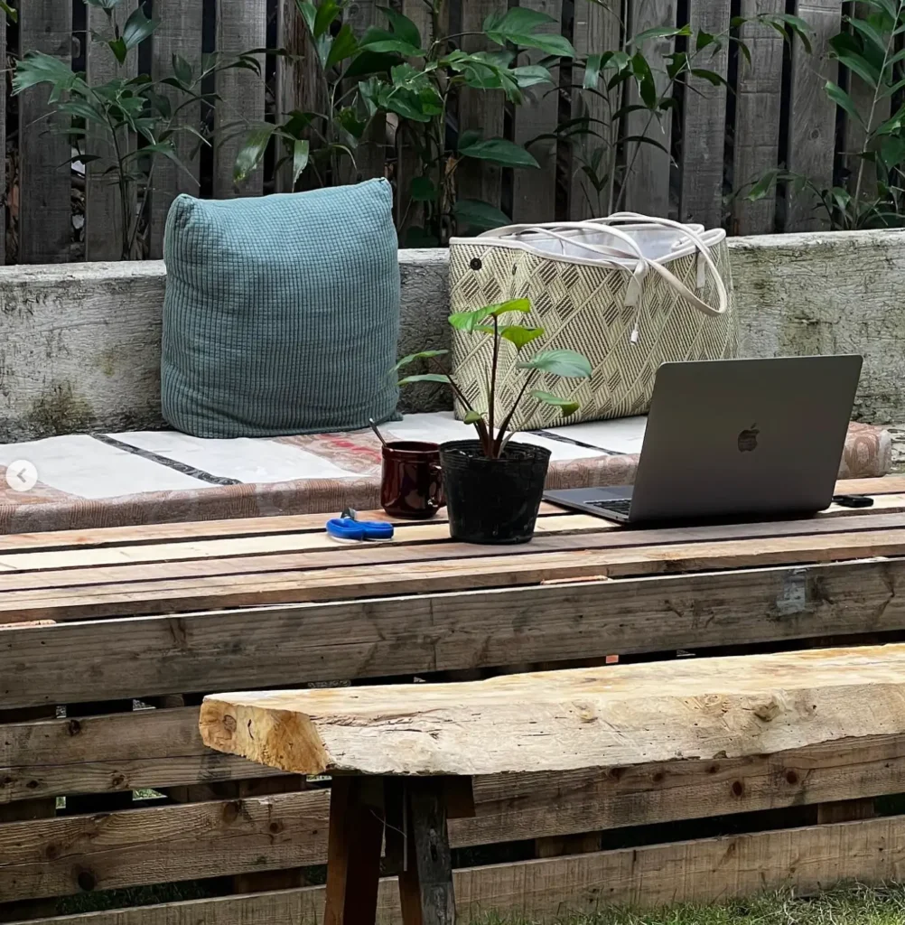Outdoor working space at Senare Boracay Hotel featuring a rustic wooden bench with a comfortable cushion, a potted plant, and a laptop setup, ideal for a tranquil work environment amidst natural greenery.