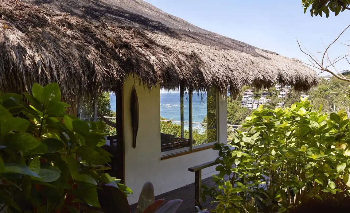 Exterior view of Sun Villa at Diniview Villa Resort in Boracay. The villa is hidden among lush tropical plants with a thatched roof and has views of the ocean.