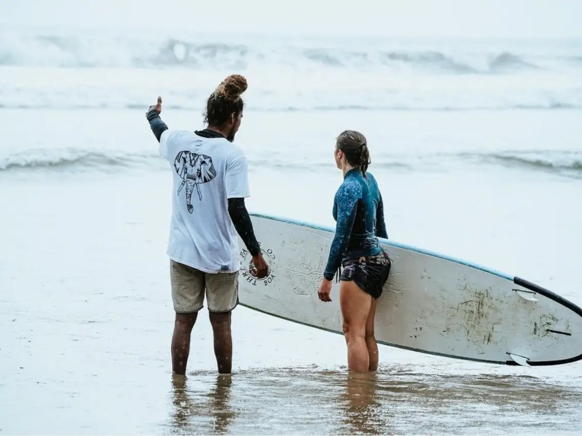 A male instructor giving tailored surfing lessons to a female student at a Surf & Yoga Bali Surf Retreat.