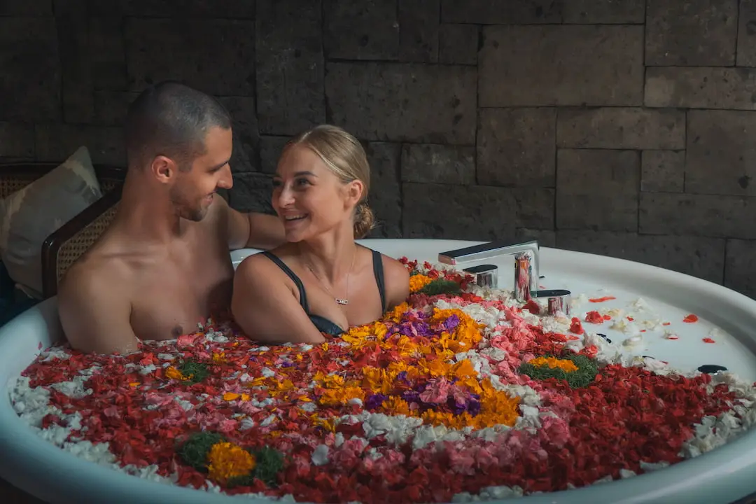 A couple enjoys a romantic moment in a circular flower bath in Bali They smile at each other, surrounded by the intimate ambiance of a dimly lit stone room.