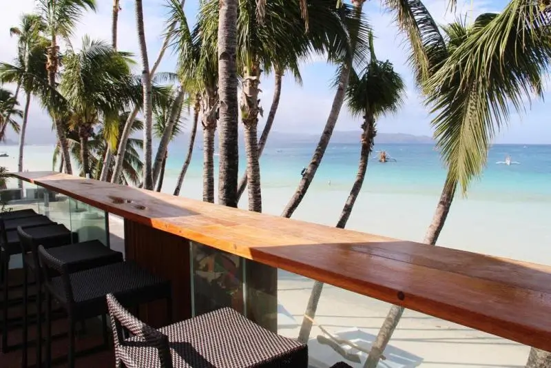 Beachfront bar at WaterColors Boracay Dive Resort, a boutique hotel in Boracay, offering stunning sea views with a long wooden counter and high stools under tall palm trees.