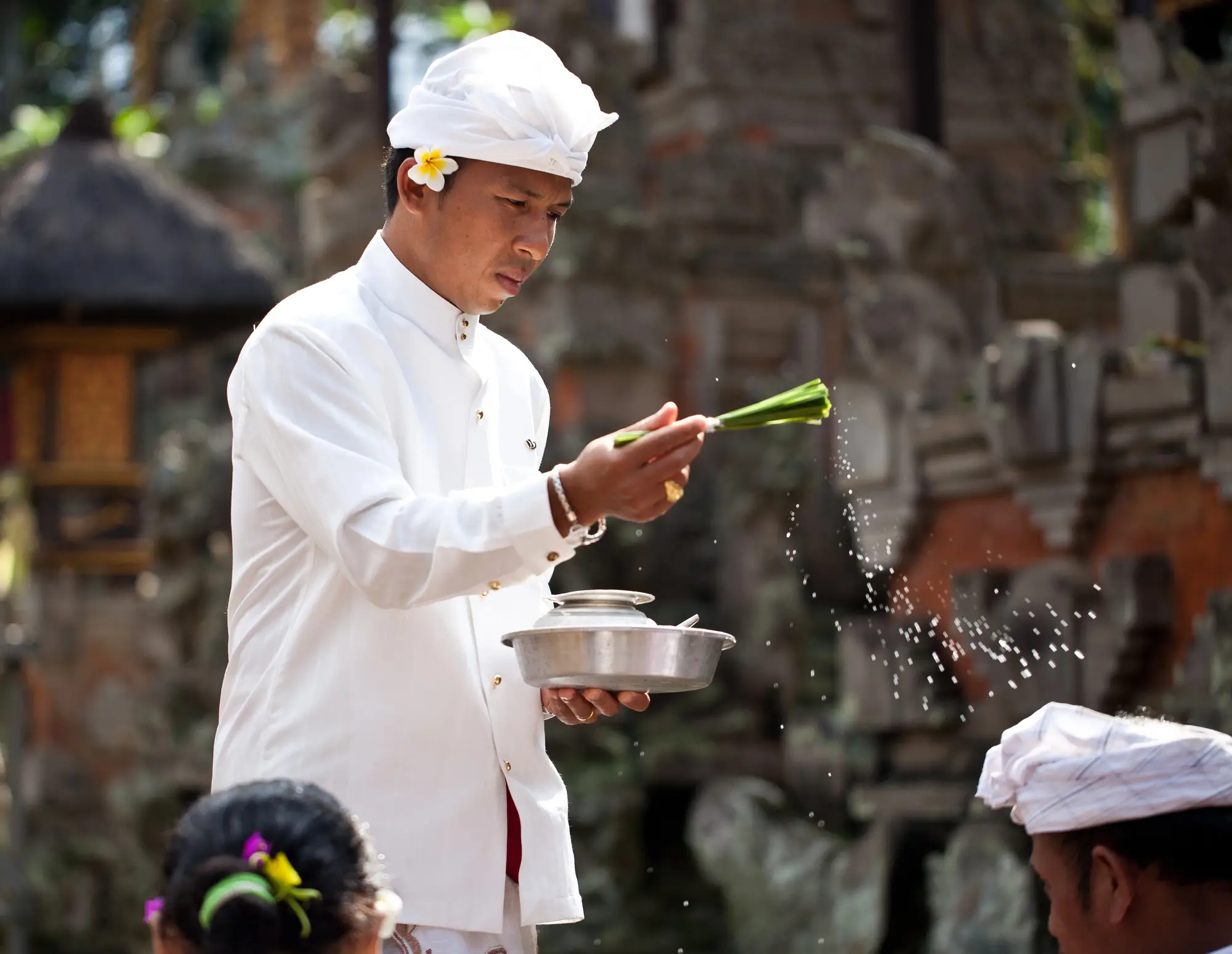 Balinese priest in white attire giving water blessings