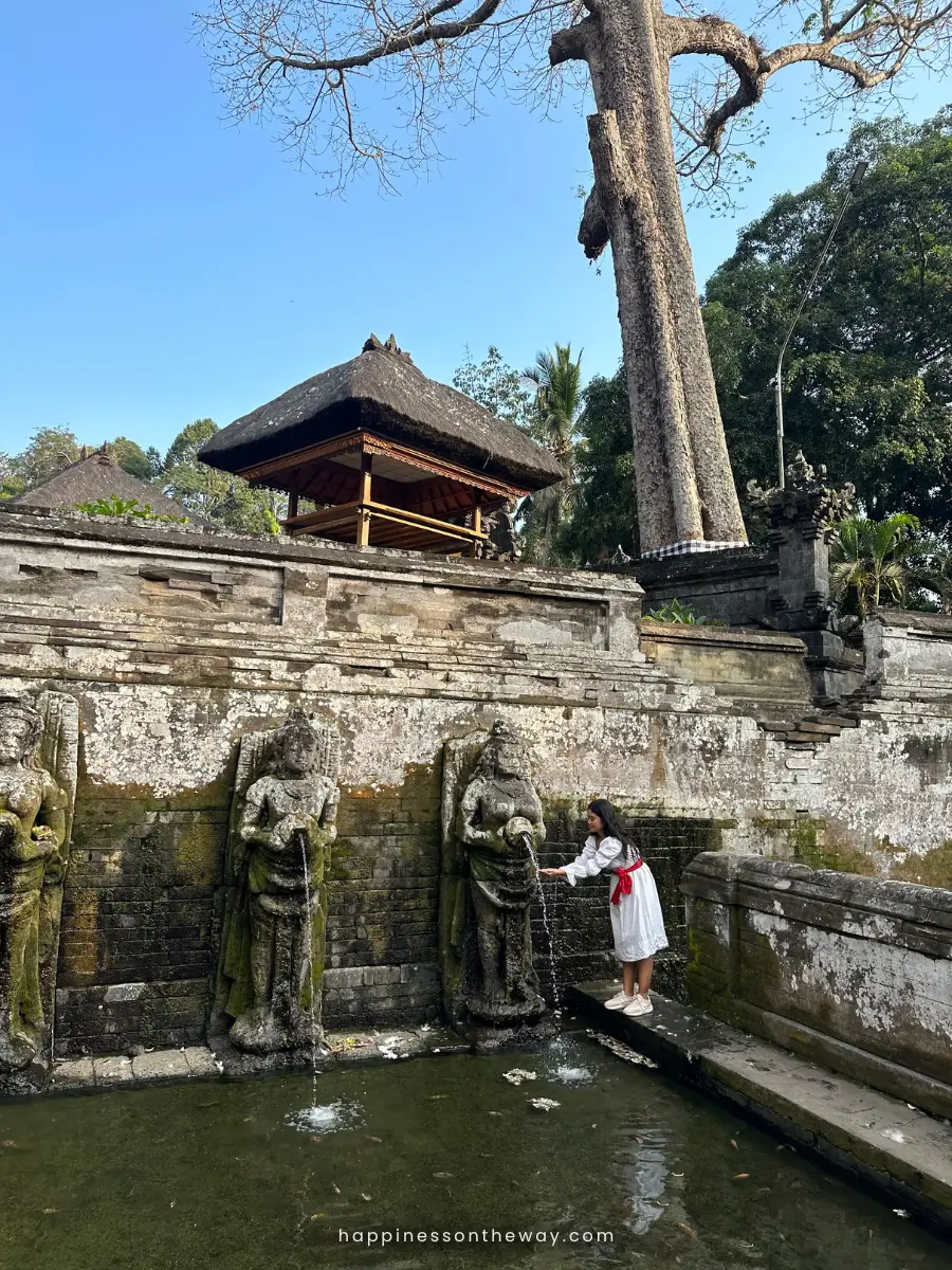 Me in a white dress getting water from a Balinese statue, one of the practices in Balinese Spirituality