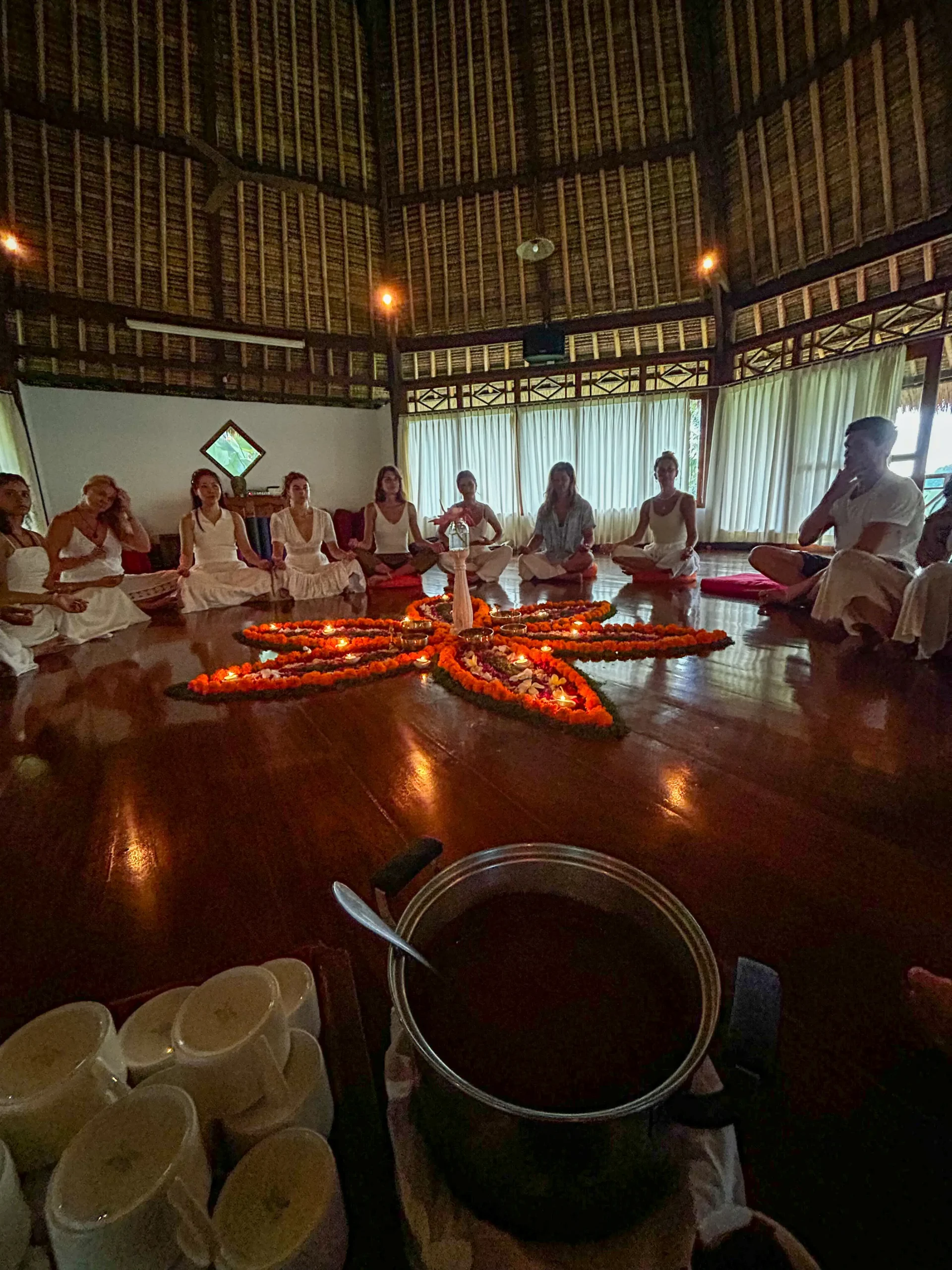 Participants gathering around a flower arrangement in Bali with cups and a pot for a cacao ceremony