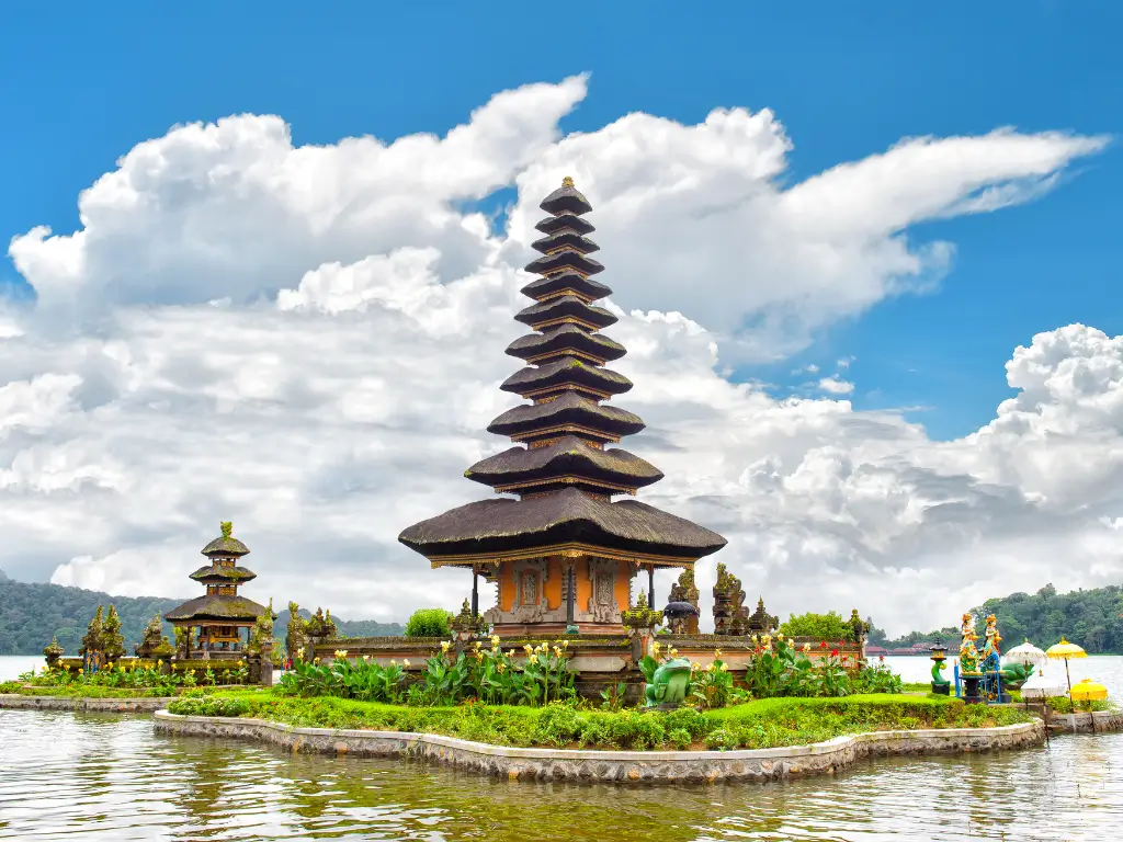 The Ulun Danu Beratan Temple, a multi-tiered pagoda structure, stands majestically on the shores of Lake Bratan in Bali, Indonesia. The temple is surrounded by lush greenery and reflects beautifully on the calm lake water, with a backdrop of dramatic, cloudy skies