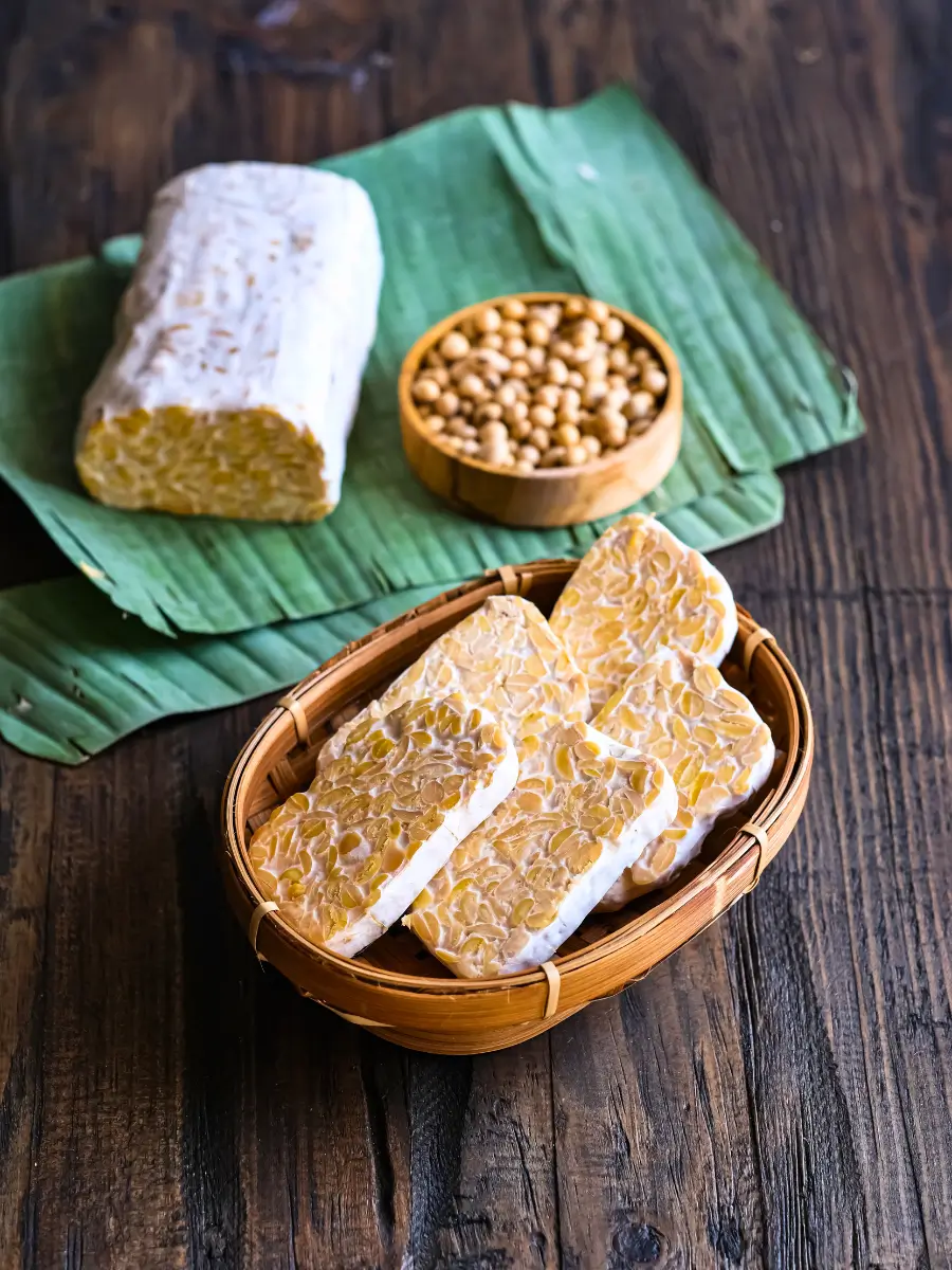 Tempeh in a bowl and on top banana leaves with a bowl of seeds