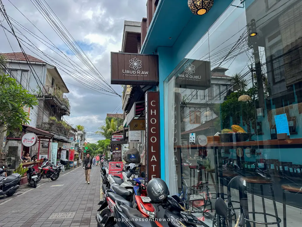 The glass and blue exterior of Ubud raw with a signage of Ubud Raw and chocolate.