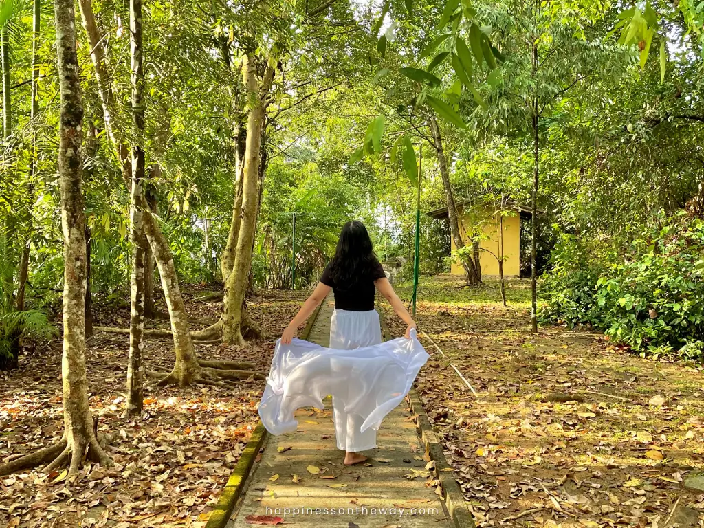 On my back with a black top and white pants holding a white shawl in a forest for my Vipassana Retreat