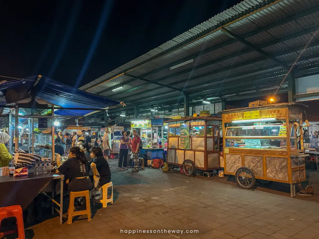 Night view of the bustling Ubud street food market, with various food stalls illuminated and people enjoying local delicacies. It's one of the best things to do in Ubud at night.