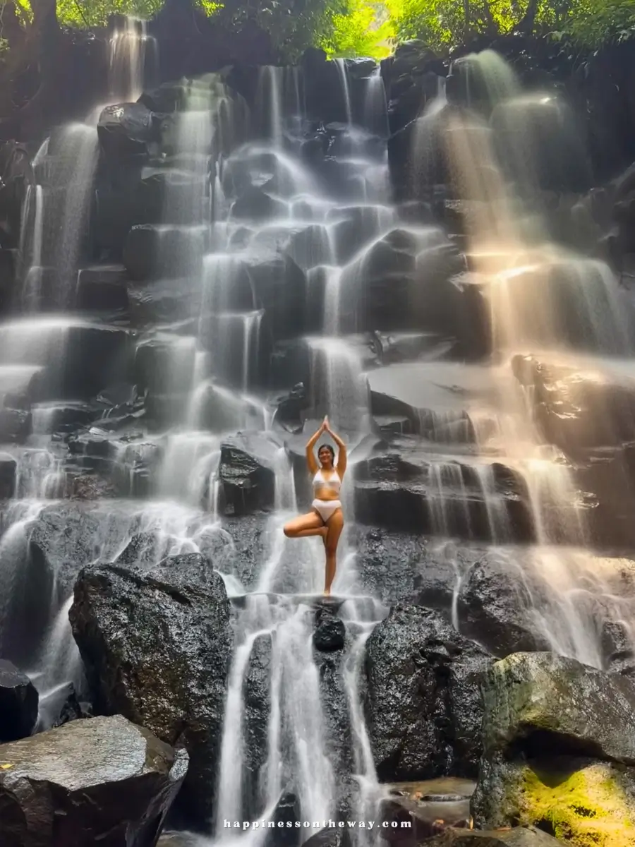 Me in a tree yoga pose standing in a terraced designed waterfall at Kanto Lampo Waterfalls, one of the famous waterfalls near Ubud.