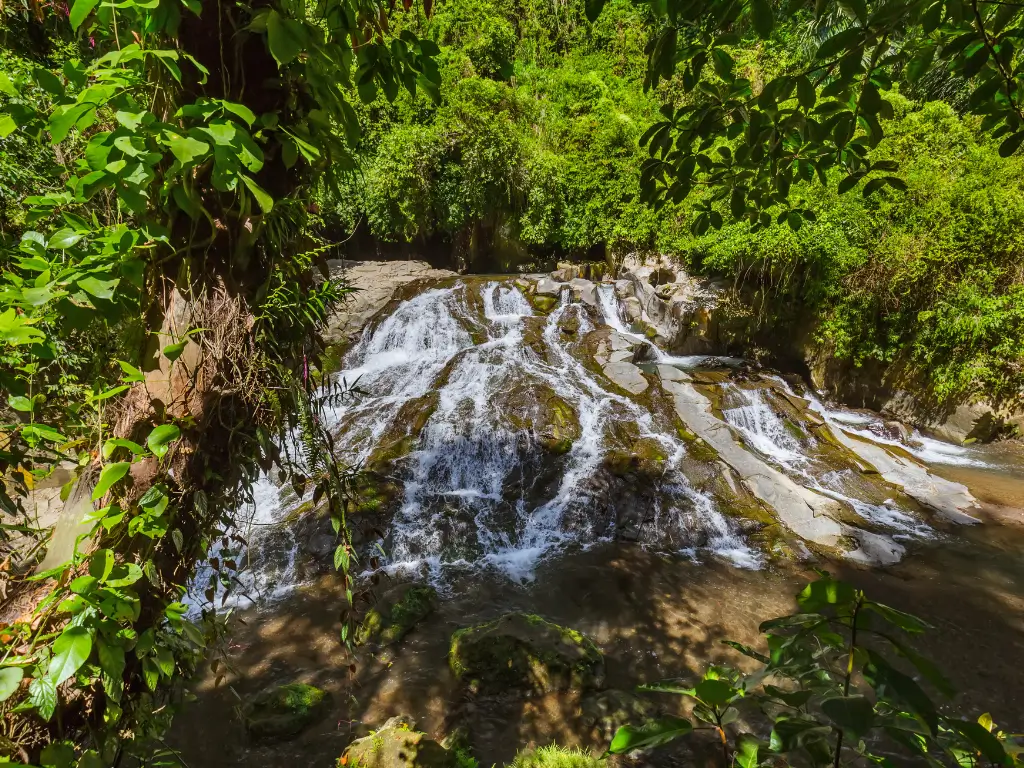 Goa Rang Reng waterfall flowing over smooth rocks surrounded by greenery in a tropical forest.