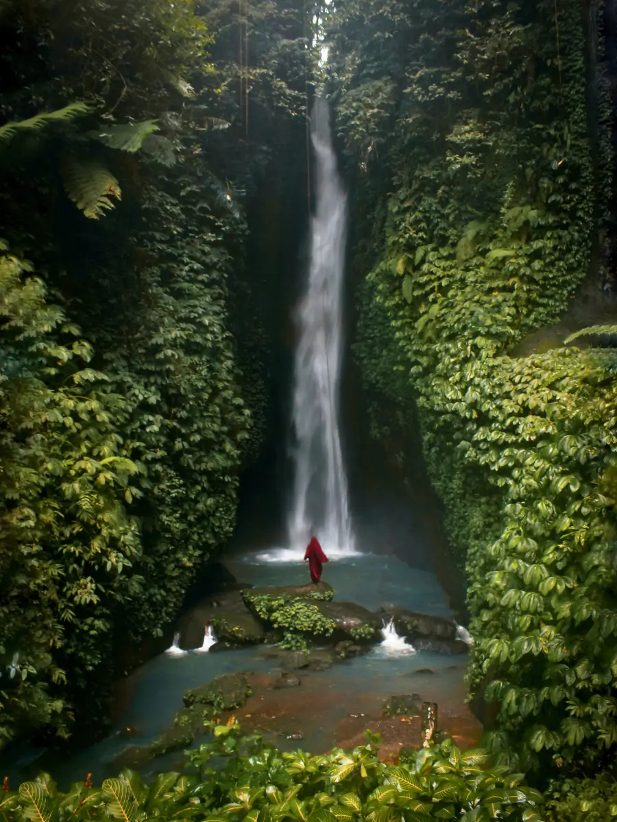 A girl in maroon ins scenic Leke Leke Waterfall flowing gracefully through a tropical paradise.