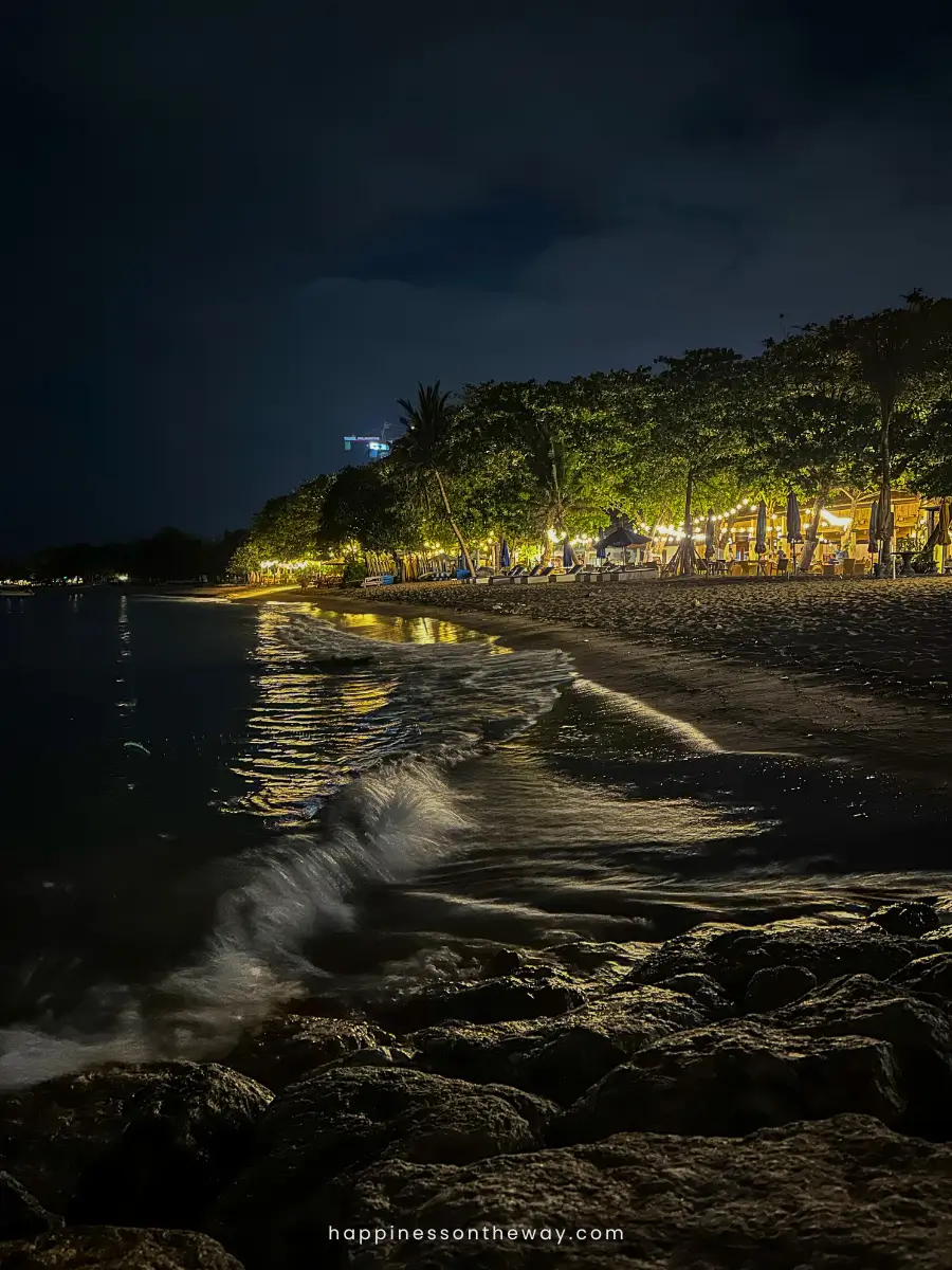 Strong waves in Sanur Beach with the lighted background of shops and restaurants at night.