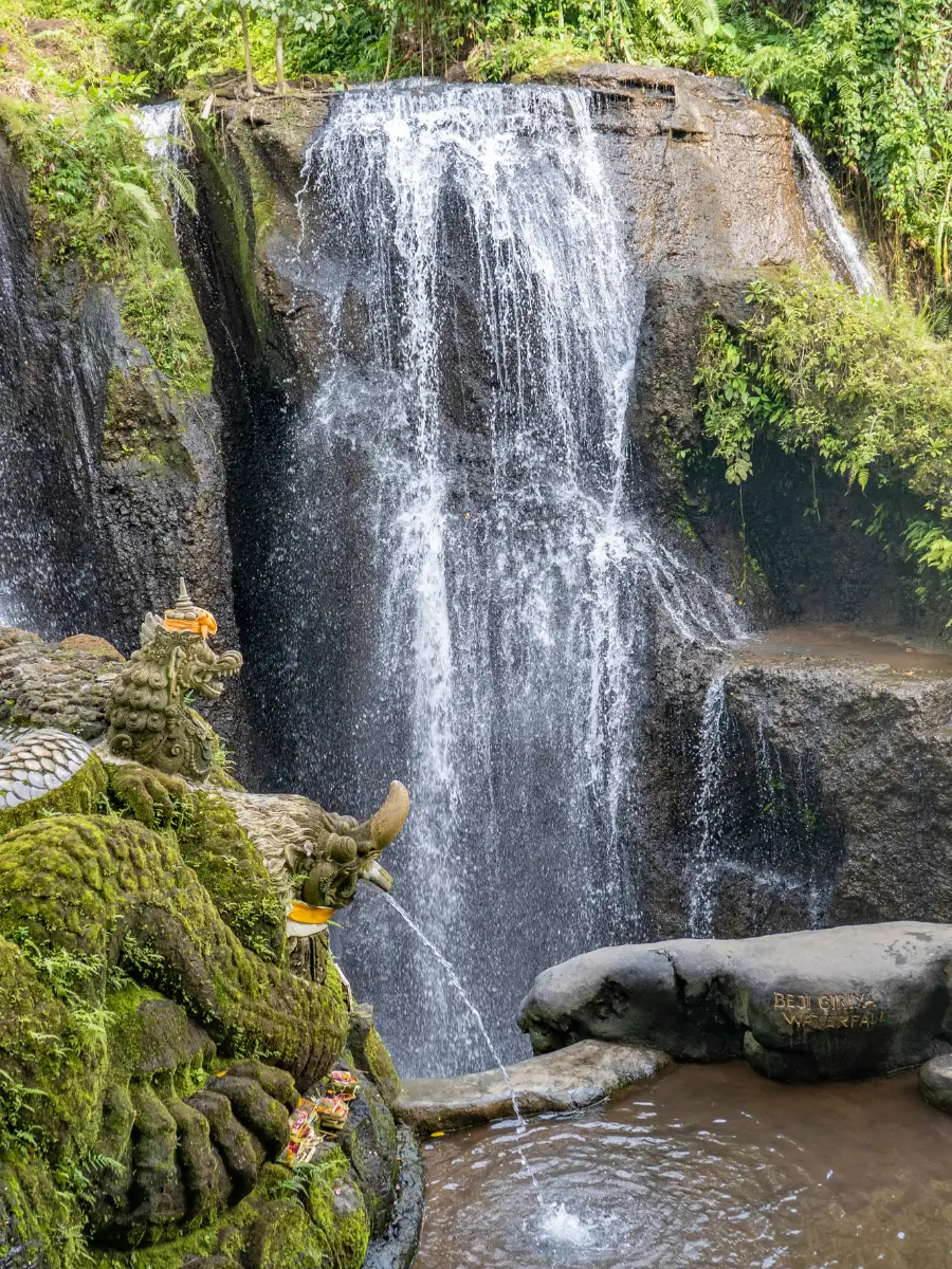 Scenic jungle waterfall Taman Beji Griya, surrounded by greenery.