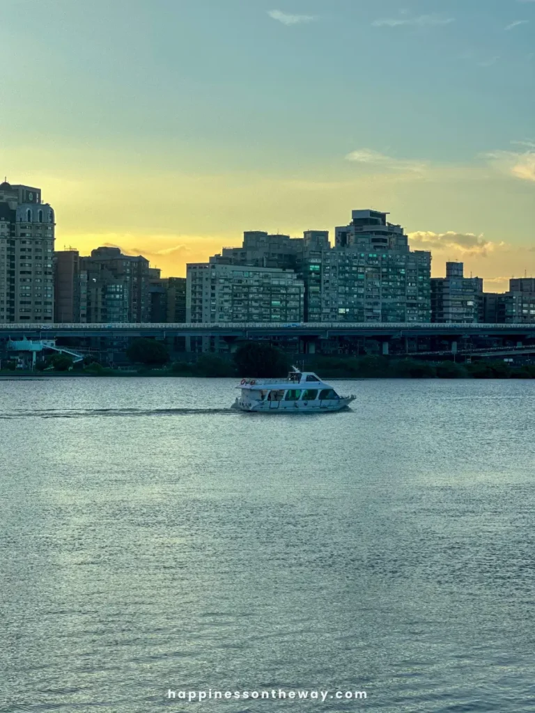 A boat sailing on the river at sunset, with the city skyline in the background at Dadaocheng Pier.