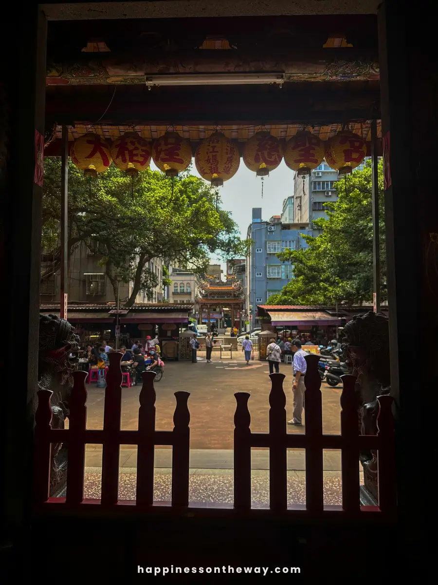 View from inside Dadaocheng Cisheng Temple looking out to the courtyard, where people are gathered and walking.