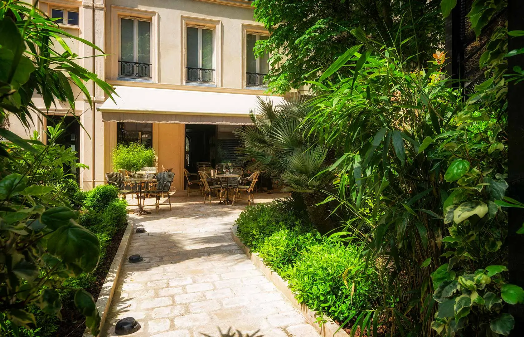 Quiet garden at B Montmartre Hotel, one of the cheap quiet hotels in Paris, with a stone path, surrounded by lush plants and outdoor seating.