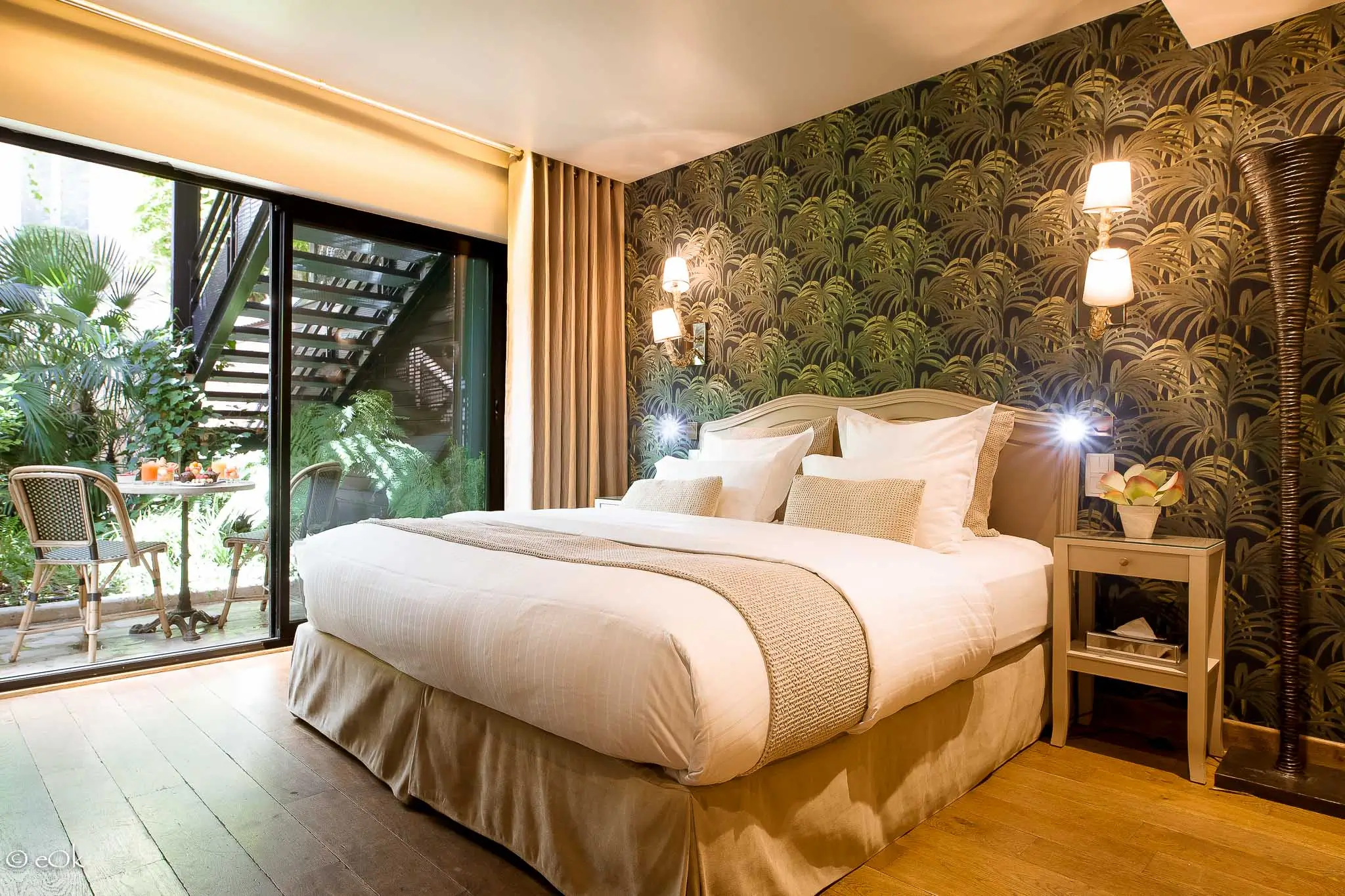 ozy bedroom at B Montmartre Hotel with a large bed, green palm-patterned wallpaper, and a private garden terrace visible through glass doors.