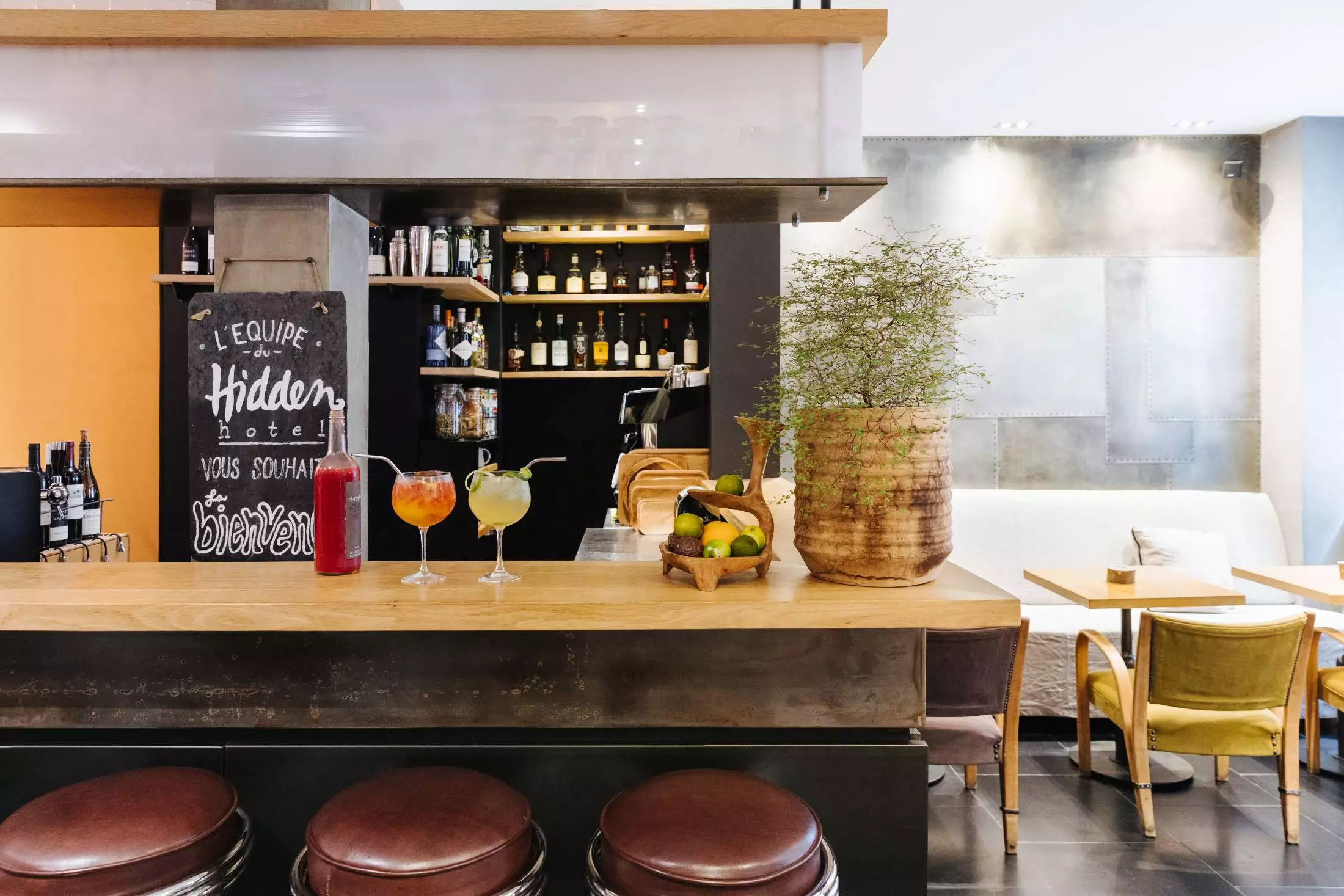 Hidden Hotel bar in Paris with a selection of cocktails on the bar table, with fruits and liquor bottles displayed on the background rack.