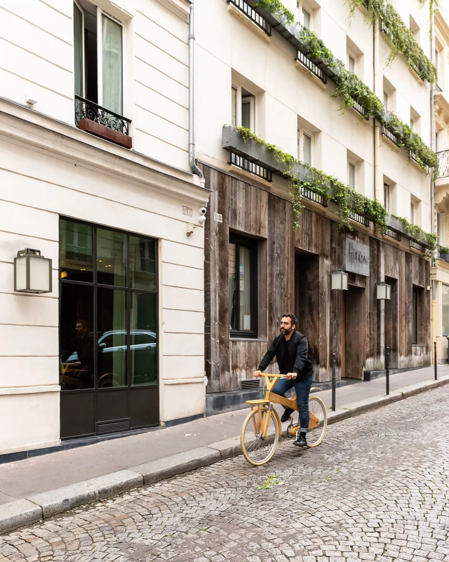 Facade of the Hidden Hotel in Paris with a wooden exterior, exuding a quiet charm, as a man on a bicycle passes by.