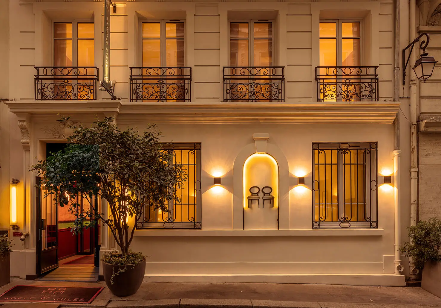 The illuminated facade of Hotel Adèle & Jules at night, with light glowing from the windows, offering a glimpse of a peaceful and quiet hotel in Paris.