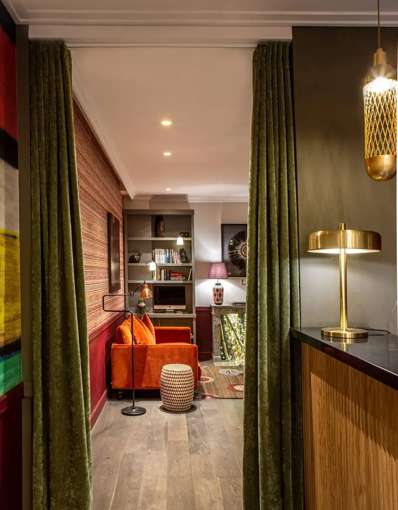 The living room of Hotel Adèle & Jules featuring a warm orange couch, elegant green curtains, and a serene ambiance.