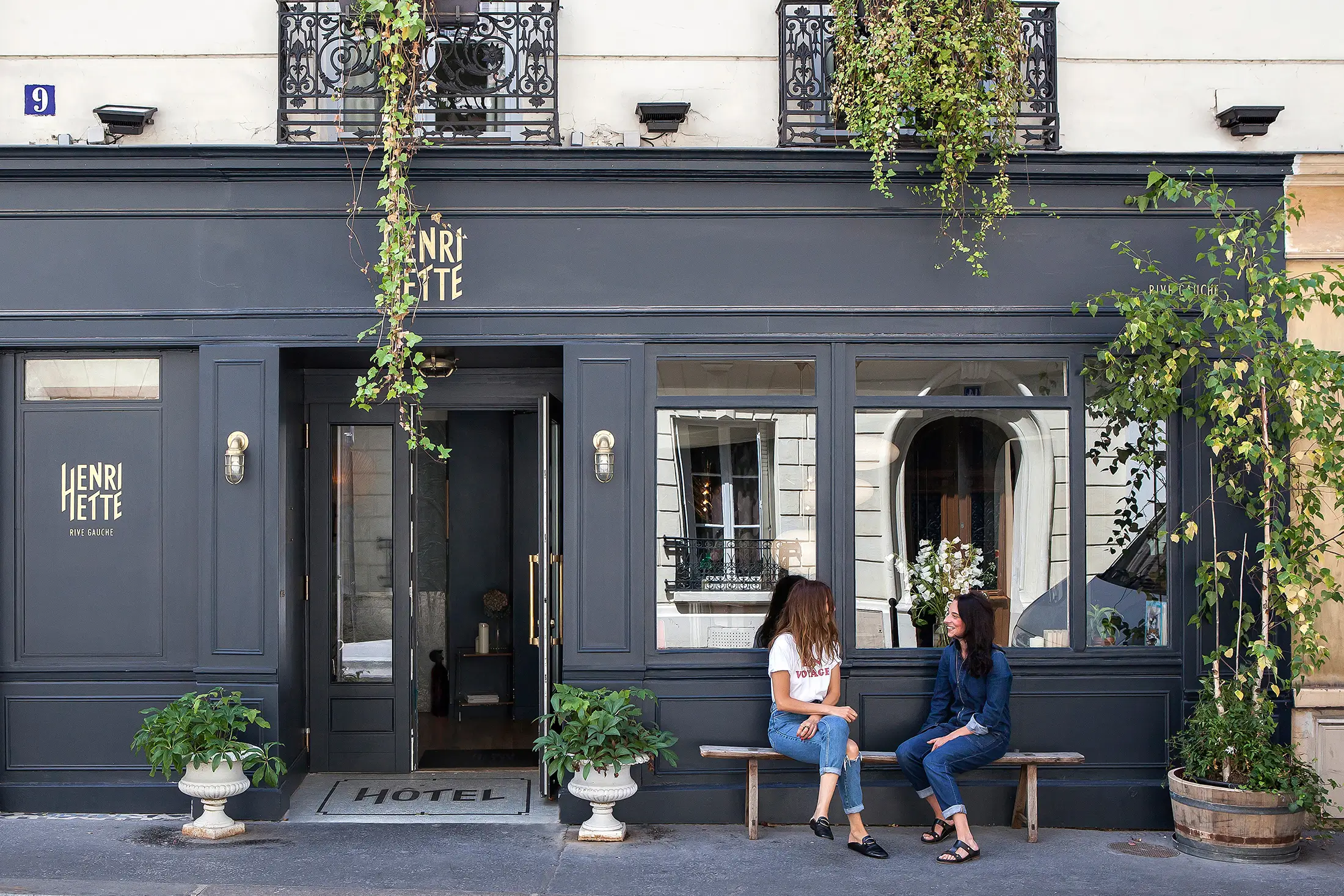 Charming facade of Hotel Henriette, a quiet hotel in Paris, with a dark gray exterior, as two girls enjoy a relaxed conversation.