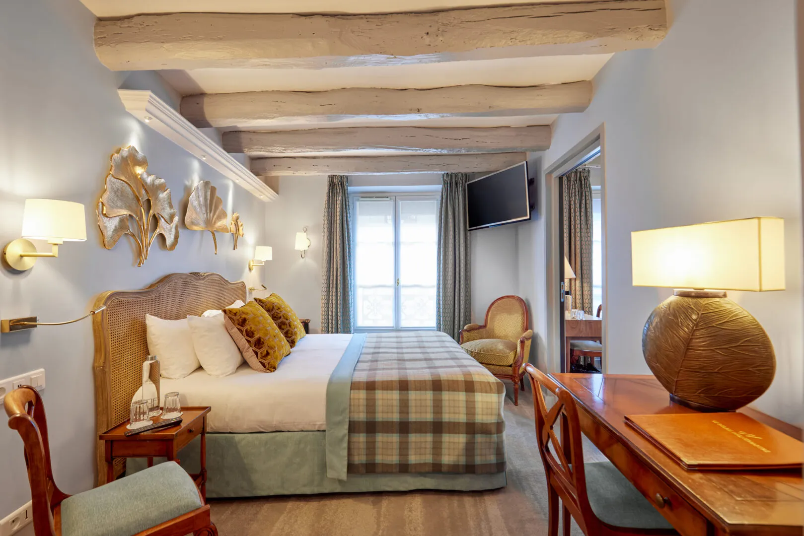 Quiet hotel in Paris, Hôtel Le Relais Montmartre bedroom with a cozy bed, a small table, and elegant wood decor on the ceiling.