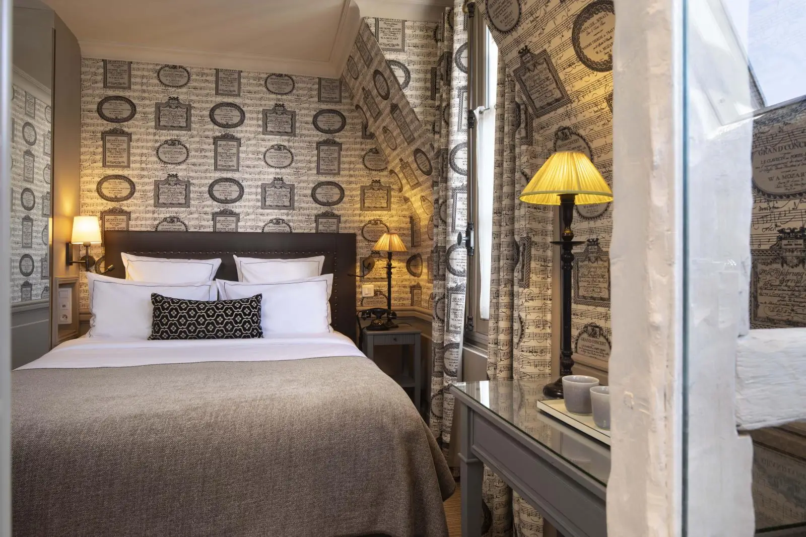 Quiet hotel in Paris showcasing a cozy room with a big, comfortable bed, gray-brown duvet, white pillows, and a yellow headstand lamp for a restful night's sleep.