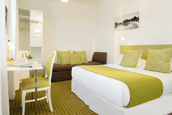 A cozy bedroom at Hotel Mistral in Paris, decorated in soft green and white tones.