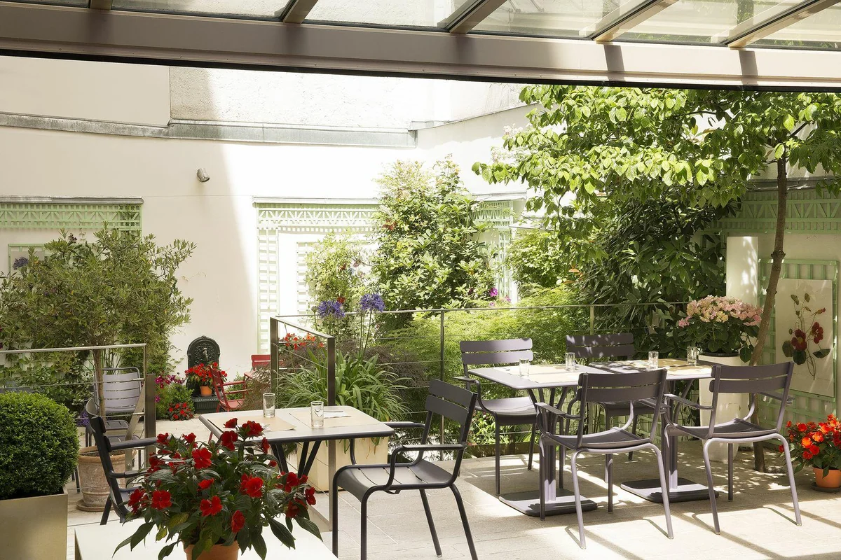 The garden at the quiet Hotel Mistral in Paris, with charming tables and chairs set amidst greenery.