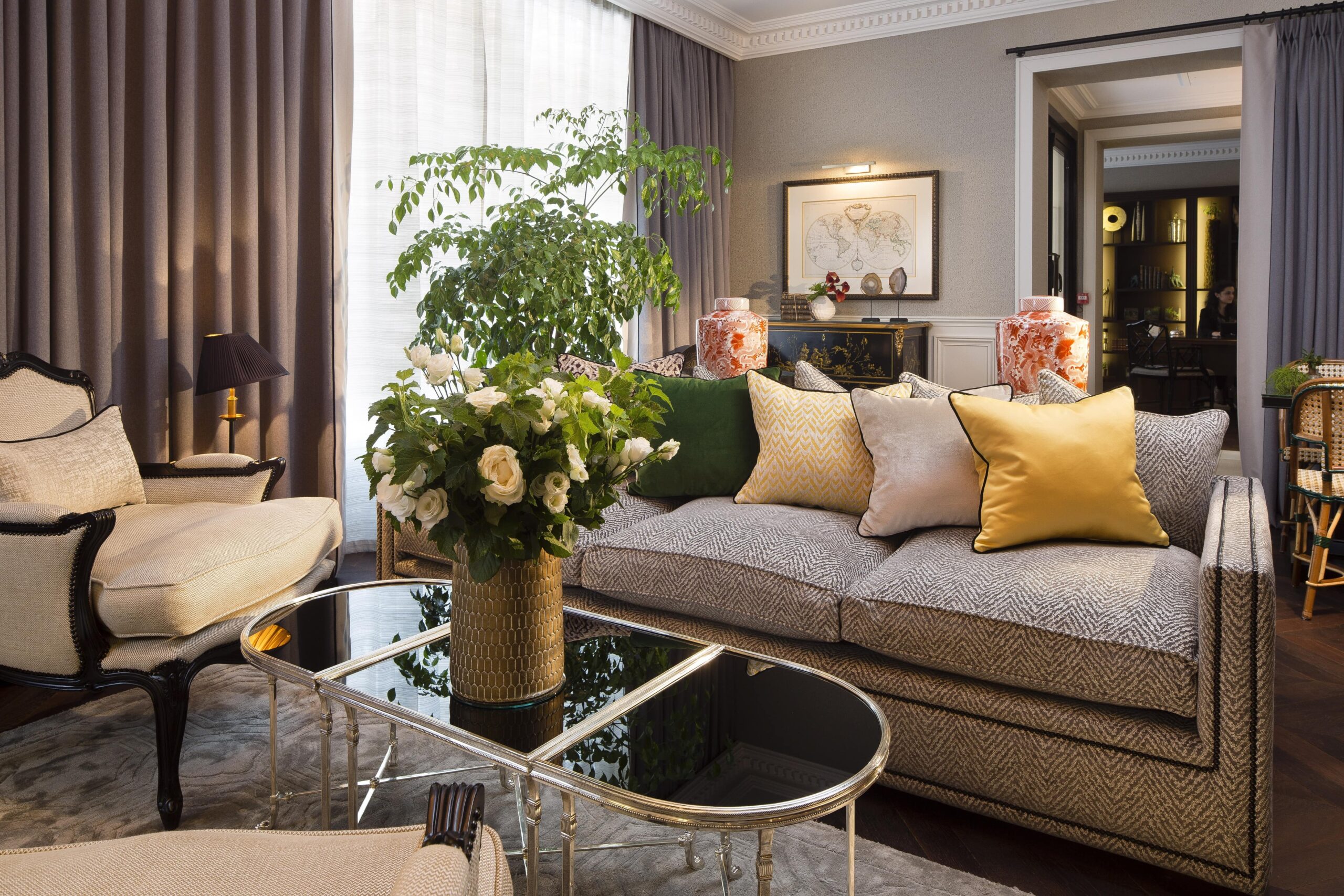 The cozy living room of Hotel Monge in Paris, showcasing a white rose vase as the centerpiece on a table, surrounded by a comfortable couch with plush pillows.