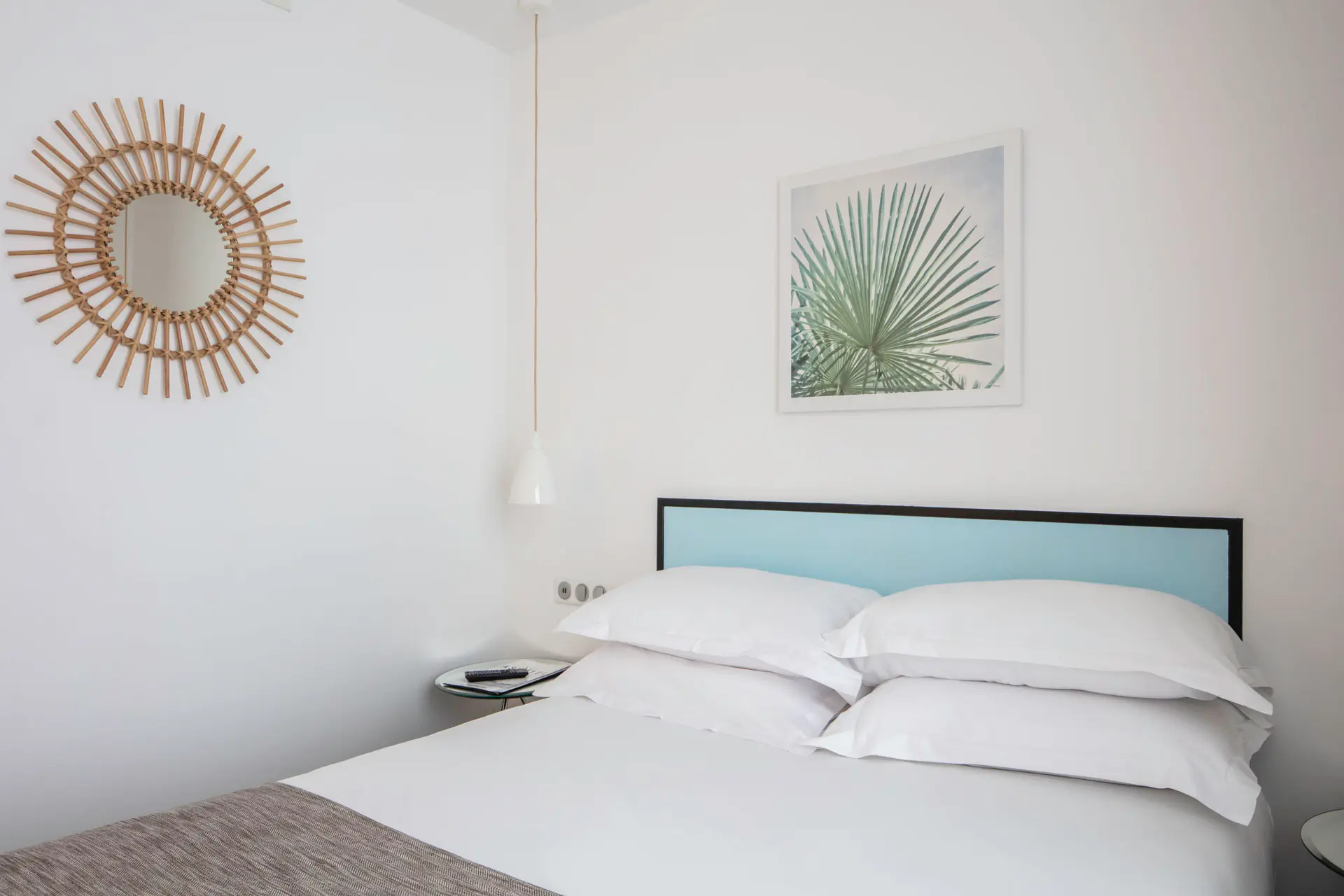 Bedroom with a comfortable bed, soft pillows, a hanging mirror, and a large leaf painting