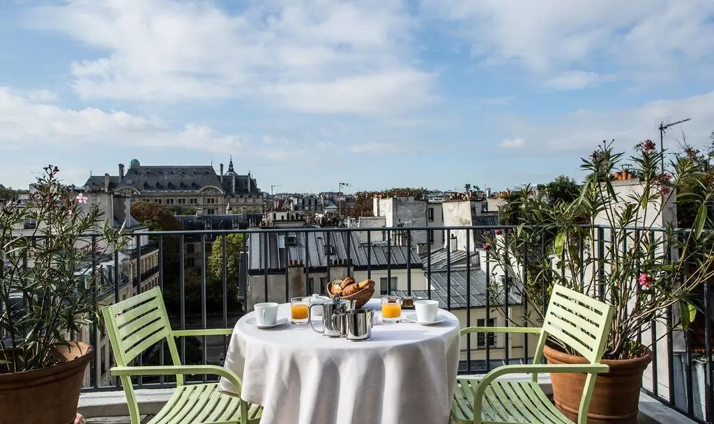 A peaceful rooftop balcony at Hotel Parc Saint Severin with a cozy set table featuring a basket of bread, coffee, and juice, offering a view of Paris.