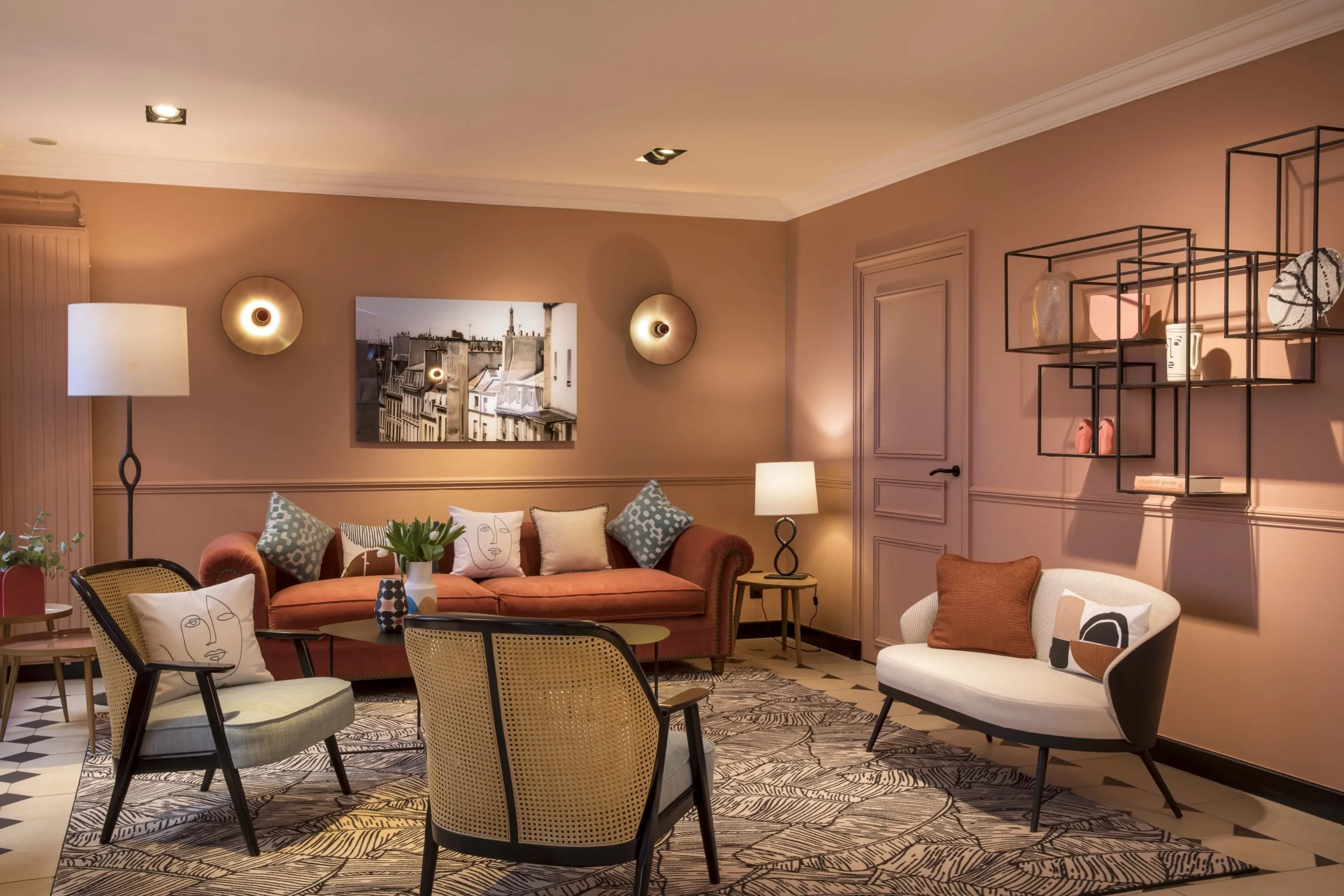 Relaxing interior at Hotel Relais Bosquet by Malone, with orange décor, comfortable chairs, a sofa, and a painting of Parisian buildings, perfect for a peaceful stay in the city.