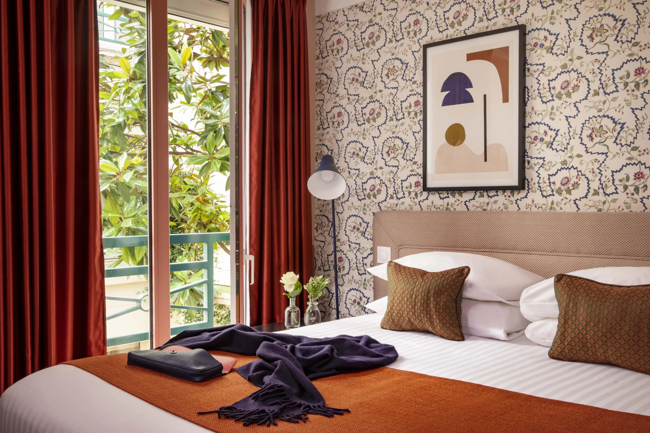 Cozy room at Hotel Relais Bosquet by Malone, featuring orange-red accents and a tranquil garden view through the glass window.