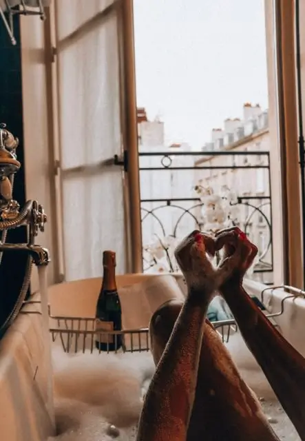 A serene moment at Hotel Saint-Marc in Paris, where hands form a heart over a luxurious bathtub filled with bubbles, accompanied by a glass of wine.