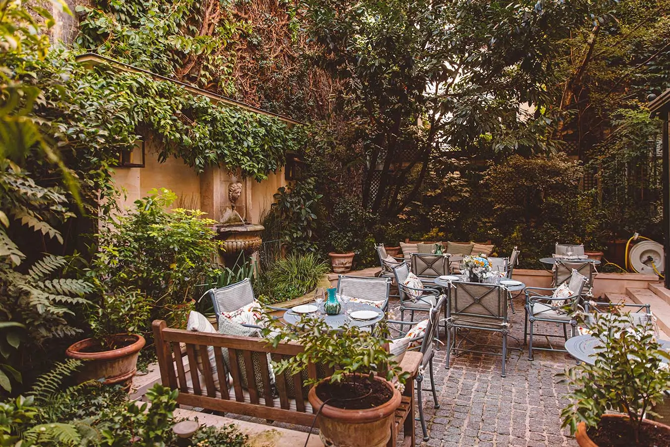 Hôtel de l'Abbaye garden, filled with lush plants and a dining table with chairs, creating a serene outdoor retreat in a quiet hotel in Paris.