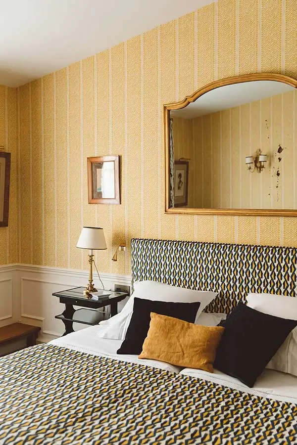 Hôtel de l'Abbaye room featuring a yellow accent wall, printed sheets, and black and yellow pillows, offering a cozy and stylish atmosphere in this quiet hotel in Paris.