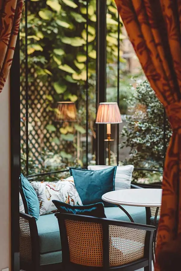 Hôtel de l'Abbaye lounge area with a blue couch adorned with pillows, positioned by a glass window that overlooks the peaceful garden, a perfect escape in this quiet hotel in Paris.