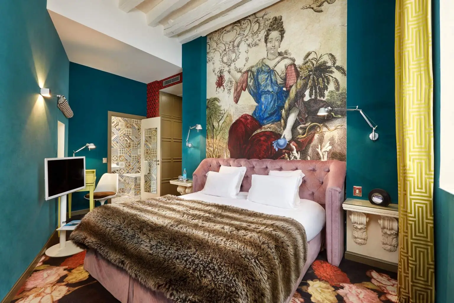 The serene, blue-toned interior of Hotel du Petit Moulin Paris, a quiet hotel in Paris, highlighted by a majestic painting of a queen above the plush seating area.