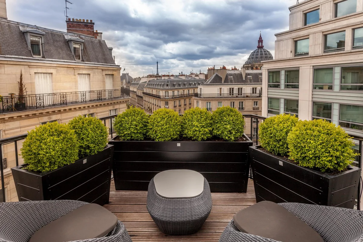 Le 12 Hotel rooftop with chairs, lush plants, and a serene view of Paris, featuring the Eiffel Tower in the distance.