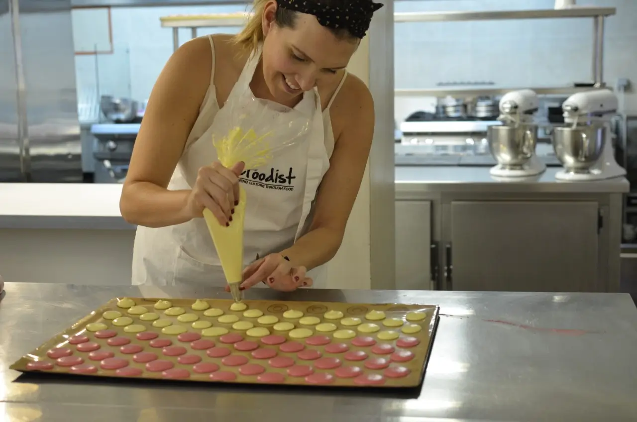 A woman wearing an apron with 'Le Foodist' piping pink and cream meringue for macarons in a pastry class in Paris