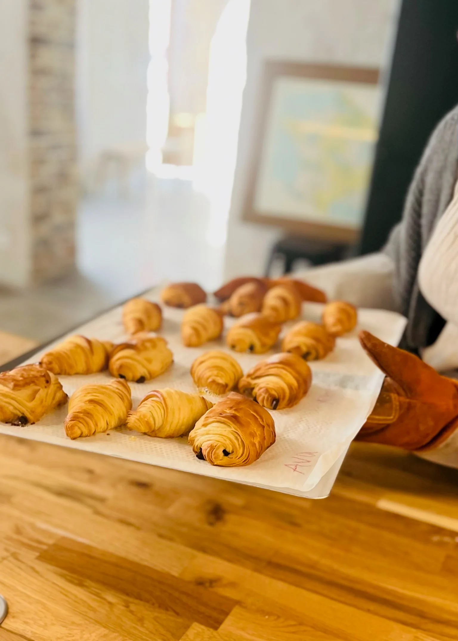 Freshly baked, golden-brown croissants on a tray, held by a person in an oven mitt at a Baking Class in Paris.
