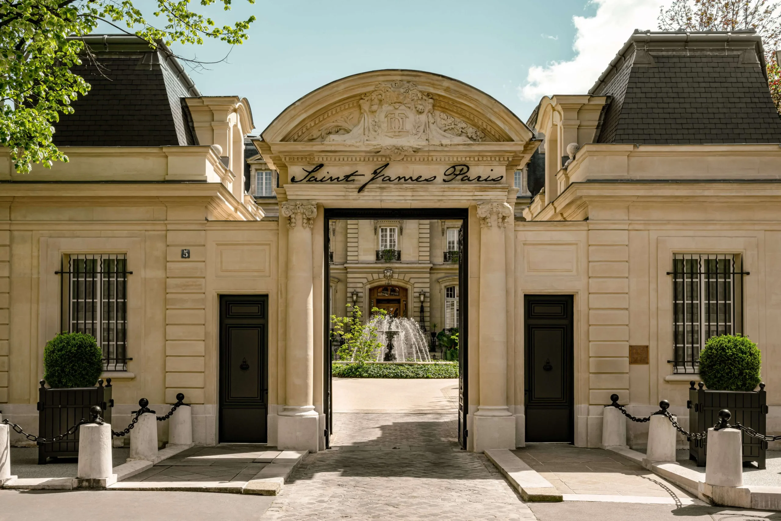 Grand entrance to the Saint James Paris hotel, with classic Parisian architecture, a fountain courtyard, and 'Saint James Paris' inscribed above the archway. A luxurious and quiet hotel in Paris.