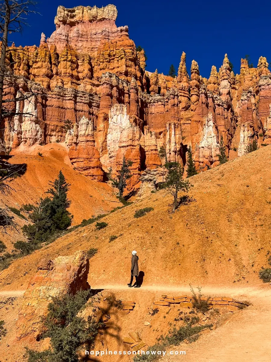 Me walking along the Queens Garden Navajo Loop trail in Bryce Canyon, surrounded by towering red rock formations under a sunny November sky.